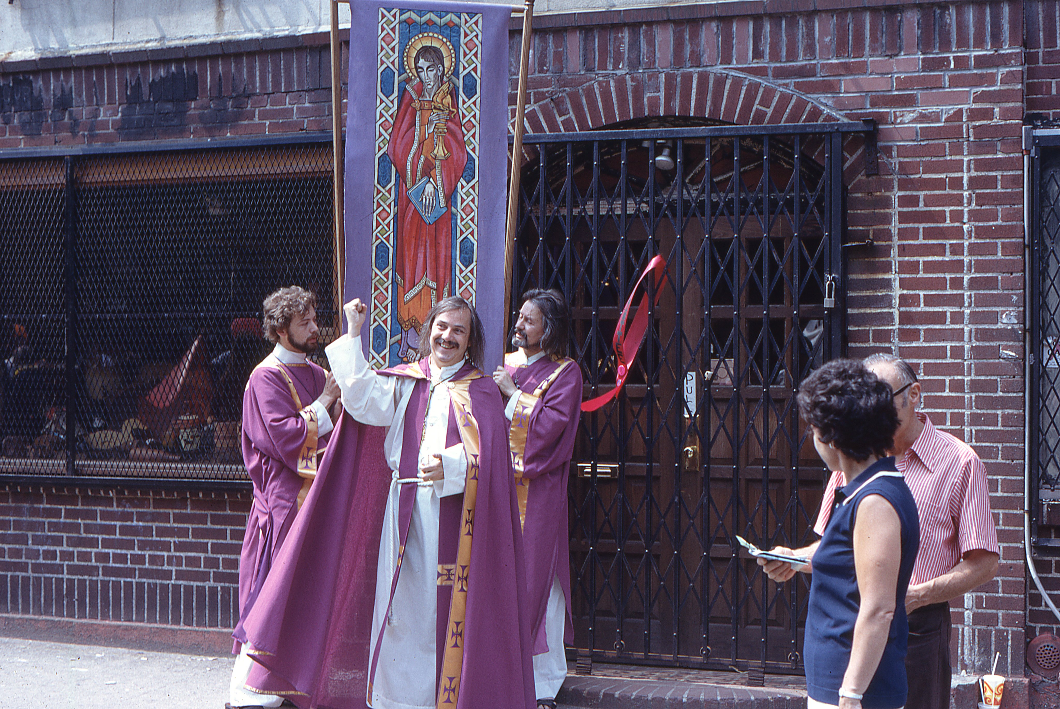 Fr. Robert Mary Clement stands outside the Stonewall Inn on Christopher Street with members of the Church of the Beloved Disciple carrying a processional banner depicting St. John the Beloved during the Fourth Annual Christopher Street Liberation Day March and Rally on June 24, 1973.