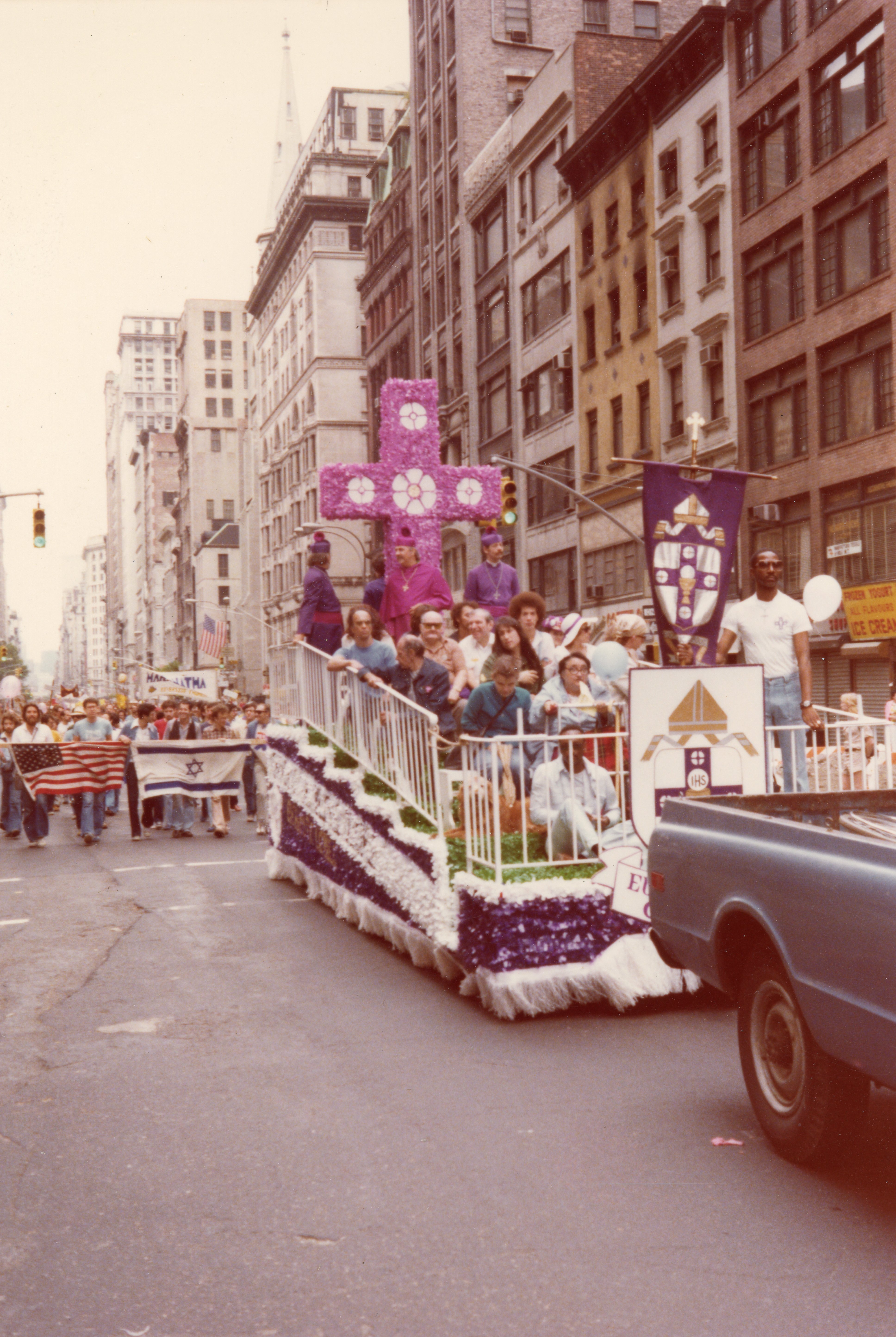 The Church of the Beloved Disciple's float during a New York City Gay Pride march, circa late 1970s - early 1980s, featured clergy in episcopal vestments beneath the congregation's distinctive floral cross. Prominently displayed was the coat of arms of the Church of the Beloved Disciple, emblazoned on purple processional banners that had become a recognizable symbol of the congregation's public ministry.