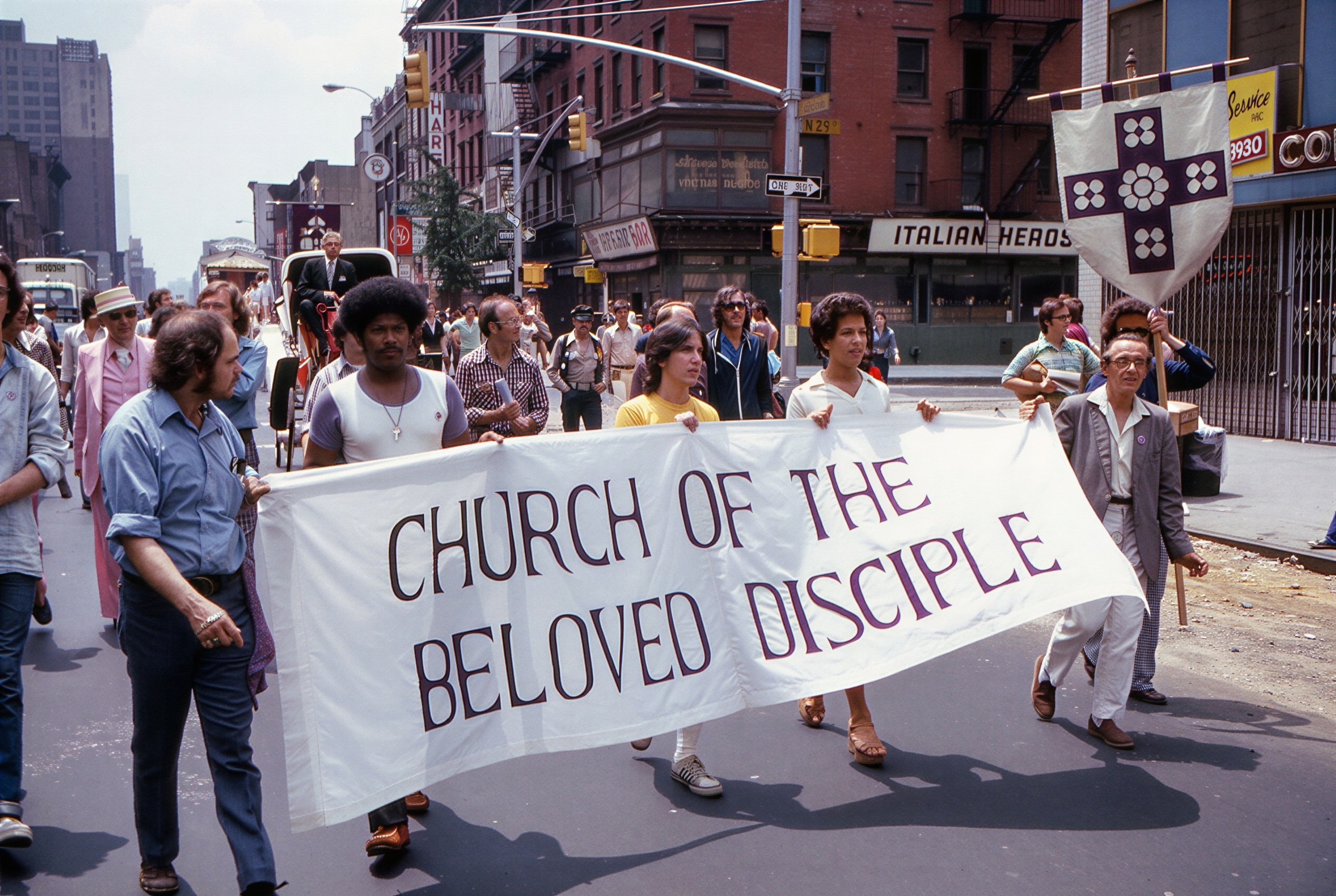 Members of the Church of the Beloved Disciple march beneath the congregation's name banner and the heraldic standard during New York City's annual Pride Parade, circa late 1970s - early 1980s. By this time, the church had become a familiar presence in Pride marches, returning each year with banners, vestments, and religious symbols that proclaimed the compatibility of Christian faith and LGBTQ identity. The procession embodied the church's enduring mission to make visible a sacramental tradition in which LGBTQ people could worship openly, celebrate their relationships, and participate fully in the life of the Church.