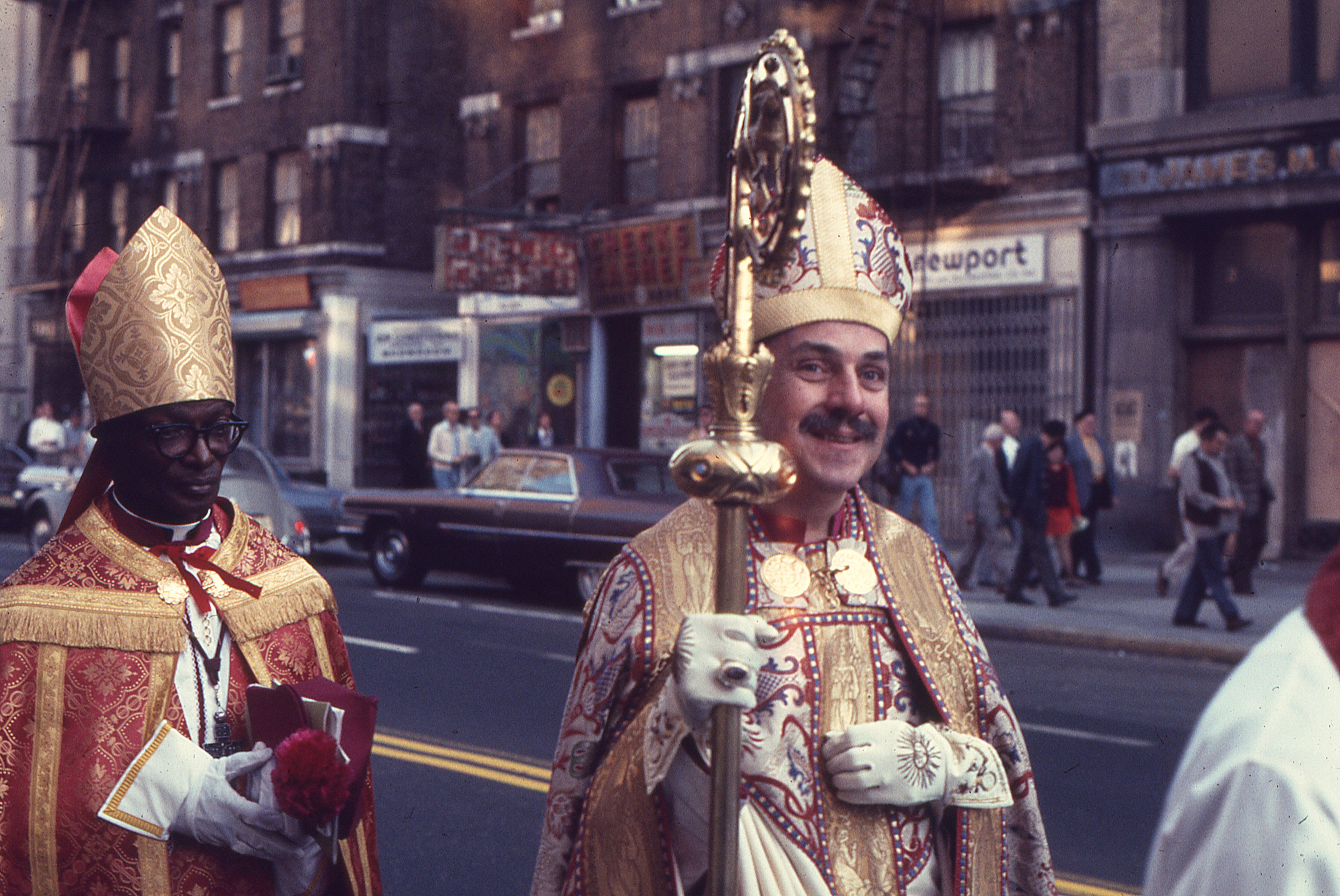 Bishop Robert Mary Clement leads the solemn procession from Metropolitan-Duane United Methodist Church at 201 West 13th Street to the Church of the Beloved Disciple at 348 West 14th Street following his episcopal consecration on October 6, 1974. At his side walks Archbishop Martin Luther Williams of the African Orthodox Church, while clergy and supporters follow behind. The public procession through the streets of Greenwich Village visibly proclaimed the Church of the Beloved Disciple's apostolic identity, carrying the celebration of Clement's consecration beyond the sanctuary and into the neighborhood it served.