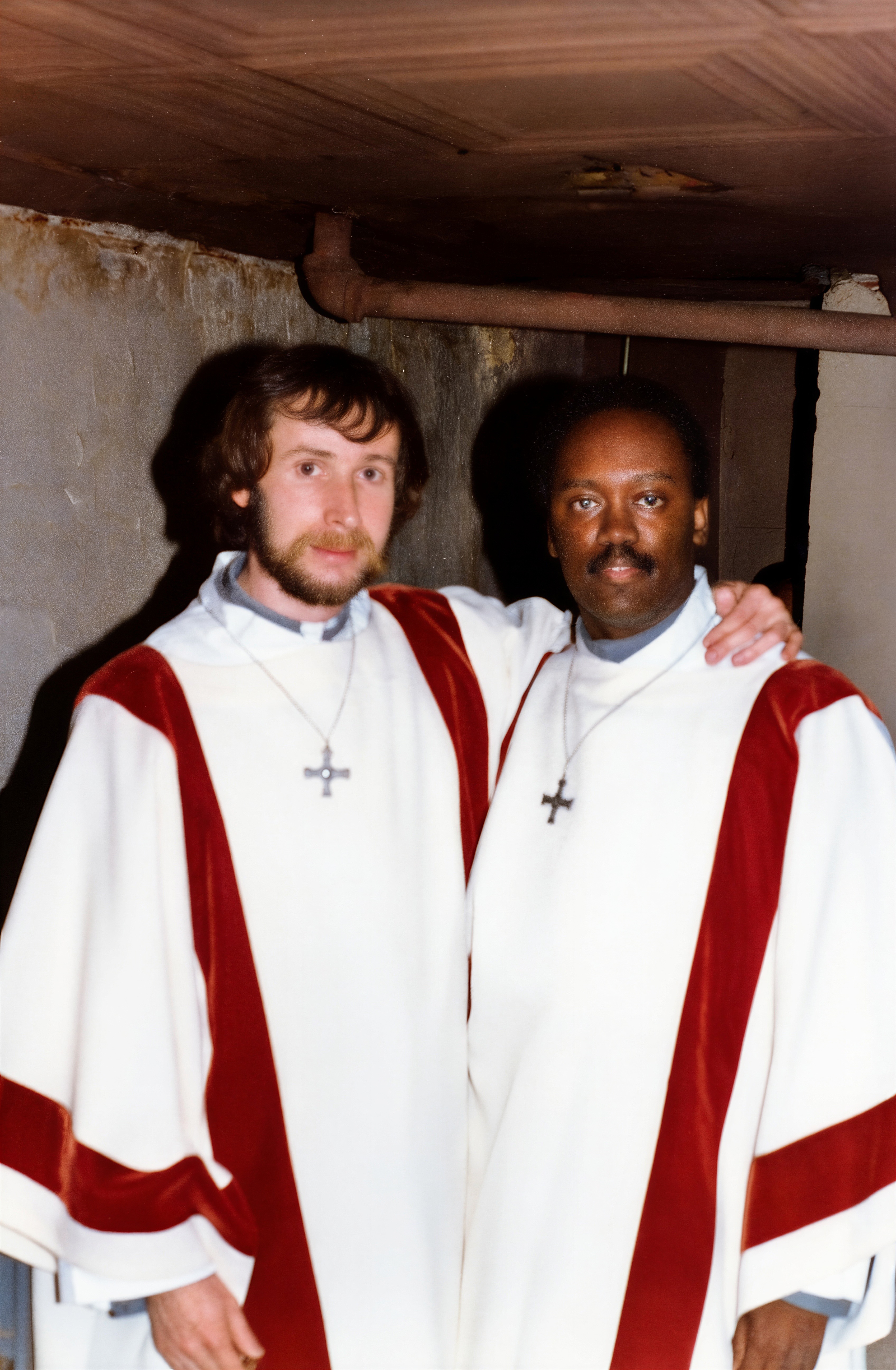 Two unidentified acolytes of the Church of the Beloved Disciple pose together before a liturgical service. Wearing white albs with red shoulder orphreys and crosses designed by the congregation, they represent the lay ministers who assisted at the church's Eucharistic celebrations and other sacramental rites. Although their names are unknown, photographs such as this document the indispensable role of volunteers whose service sustained the parish's worship and communal life.