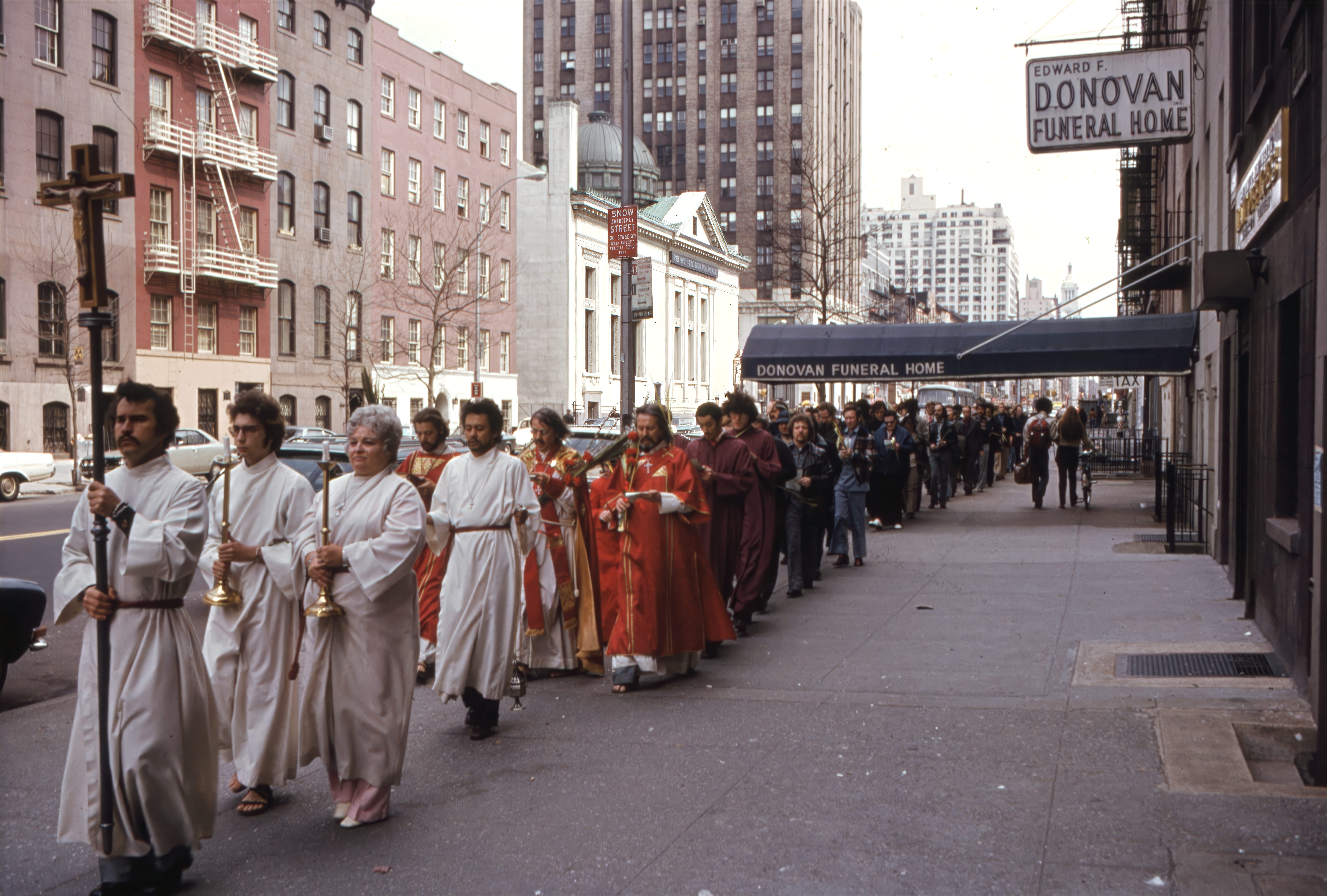 Clergy, acolytes, and parishioners of the Church of the Beloved Disciple process through the streets of Manhattan on Palm Sunday, retracing Christ's entry into Jerusalem with prayer, hymns, and the processional cross. Led by Archbishop Robert M. Clement and the church's clergy, the procession carried the liturgy beyond the sanctuary, making the church's presence visible in the city's neighborhoods. For the congregation, these annual public processions affirmed both the continuity of Catholic tradition and the conviction that LGBTQ Christians belonged fully within the Church's sacramental life.