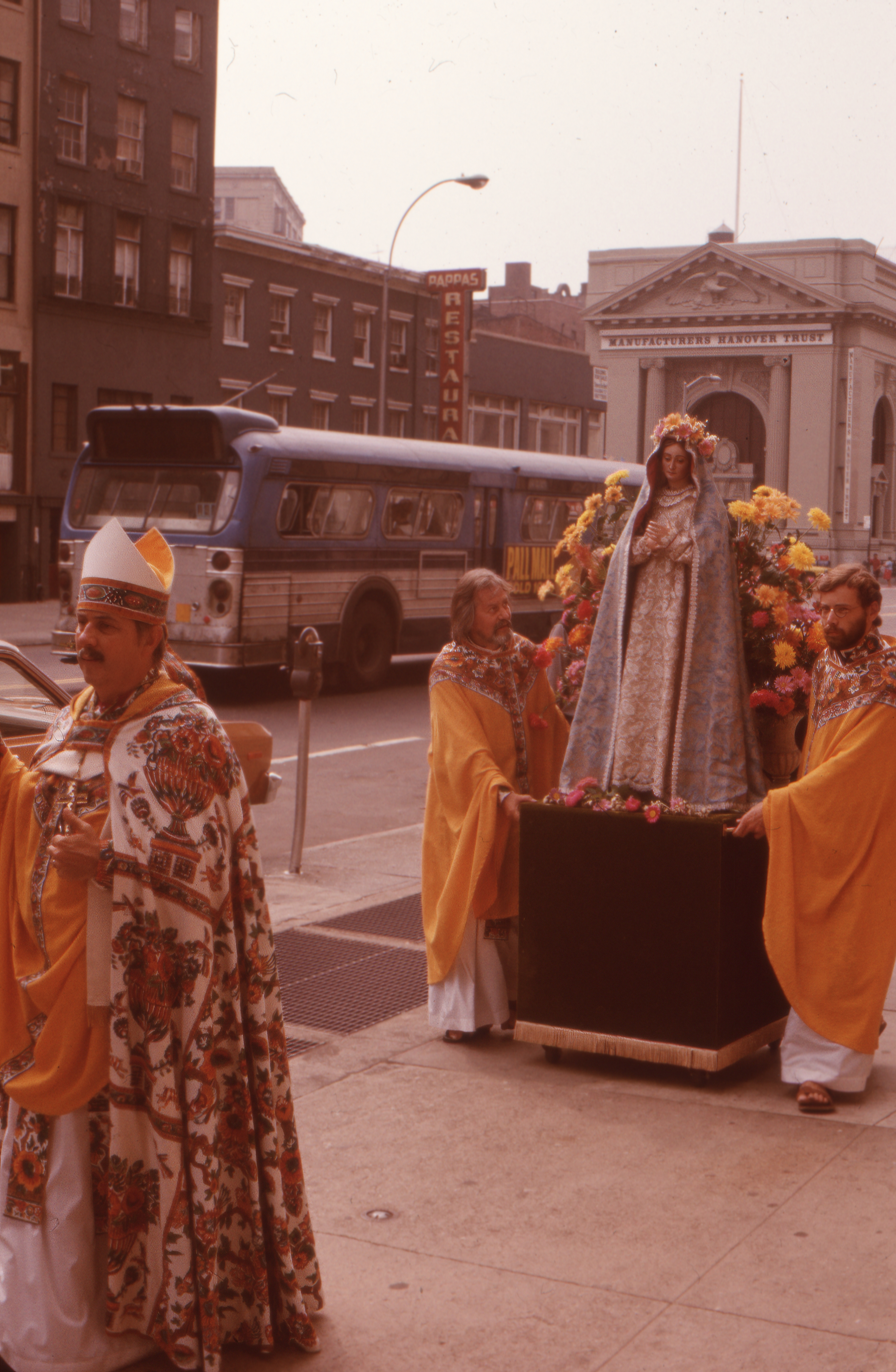 Archbishop Robert M. Clement leads the Church of the Beloved Disciple's procession for the Feast of the Assumption of the Blessed Virgin Mary as clergy carry a flower-decked statue of the Virgin through the streets of Manhattan. By bringing one of the Church's principal Marian feasts into the public square, the congregation affirmed its deep devotion to Mary while demonstrating that LGBTQ Christians fully shared in the traditions of Catholic faith and worship. These annual processions expressed the Church of the Beloved Disciple's conviction that sacred ritual belonged not only within the sanctuary but also in the life of the city.