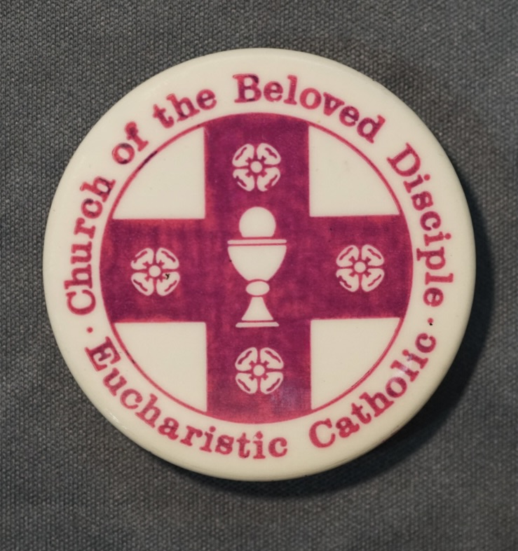 This small metal button bearing the name and emblem of the Church of the Beloved Disciple was produced as an identifying badge for members and supporters of the congregation. The design features the church's distinctive seal: a cross surrounding a Eucharistic chalice surmounted by the Sacred Host, accompanied by four stylized rosettes and the inscription "Church of the Beloved Disciple – Eucharistic Catholic." Worn at parish events, public processions, ecumenical gatherings, and LGBTQ demonstrations, the button served as a portable expression of the church's identity, publicly proclaiming both its sacramental tradition and its ministry of welcome and affirmation. Today it survives as a rare piece of material culture documenting one of America's earliest openly LGBTQ-affirming Catholic communities.