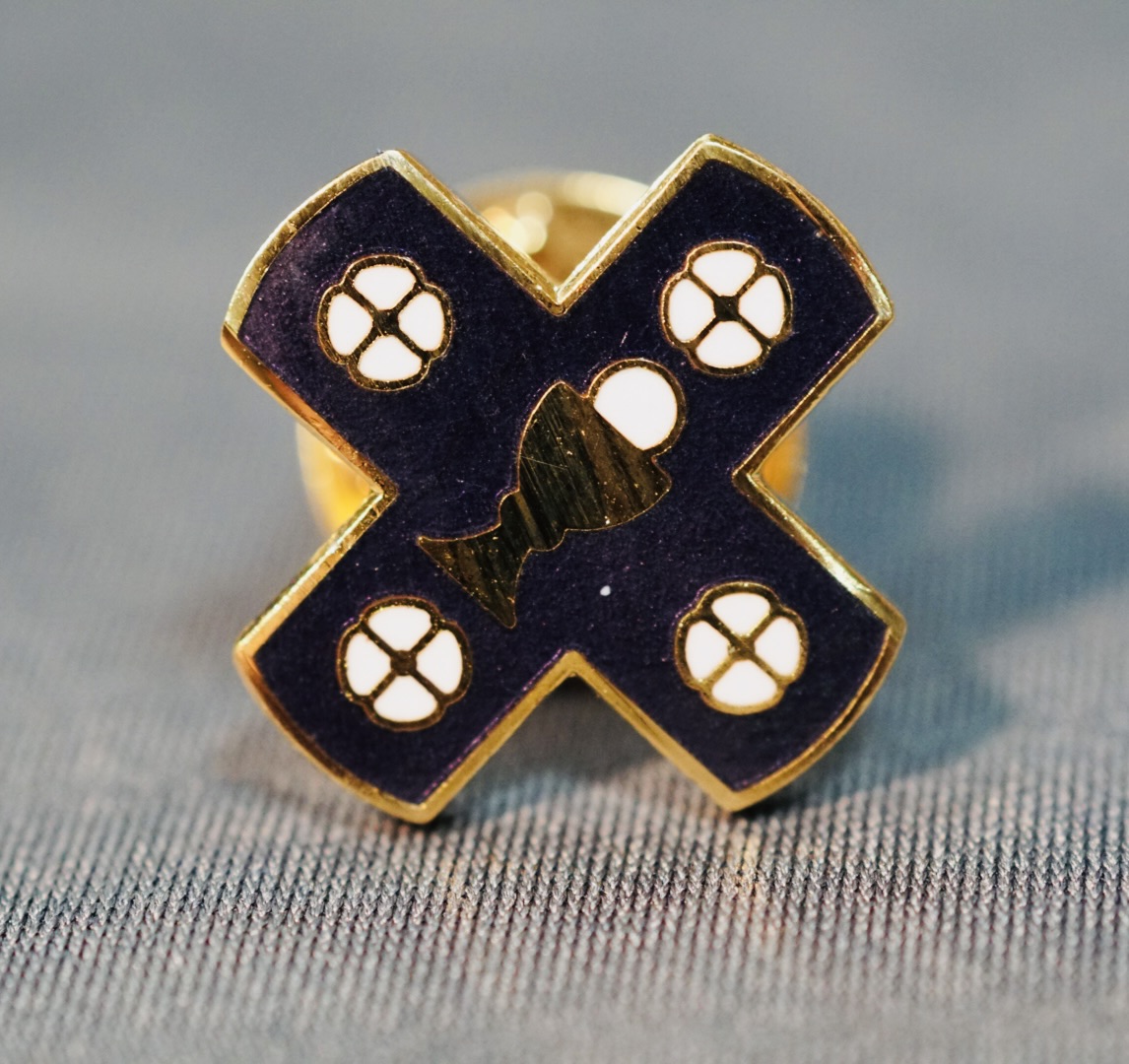 This small enamel lapel pin reproduces the official emblem of the Church of the Beloved Disciple in the form of a cross. At its center, a Eucharistic chalice surmounted by the Sacred Host proclaims the church's sacramental identity, while four stylized quatrefoils occupy the spaces between the arms of the cross. Worn by clergy, members, and supporters, the pin served as a discreet yet recognizable expression of affiliation with the congregation. Its compact form made it suitable for everyday wear as well as for liturgical celebrations, public processions, ecumenical gatherings, and LGBTQ+ community events, embodying the church's distinctive witness as an openly affirming sacramental community rooted in Eucharistic devotion.